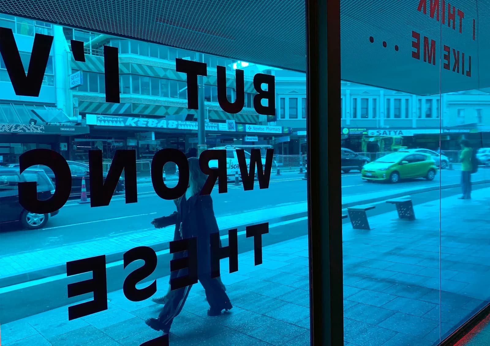 Karangahape Road reflected in reverse in the electric-blue glass of a gallery window