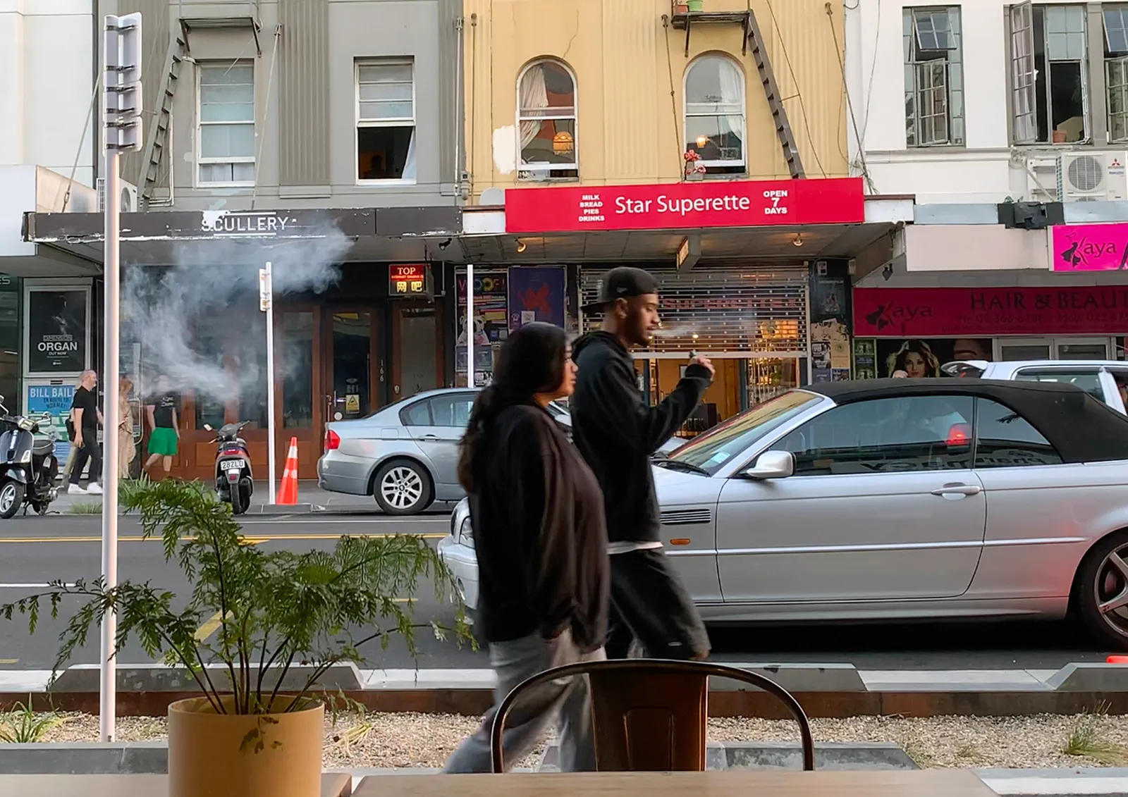 Two people walk past Star Superette as smoke drifts across the K Road footpath