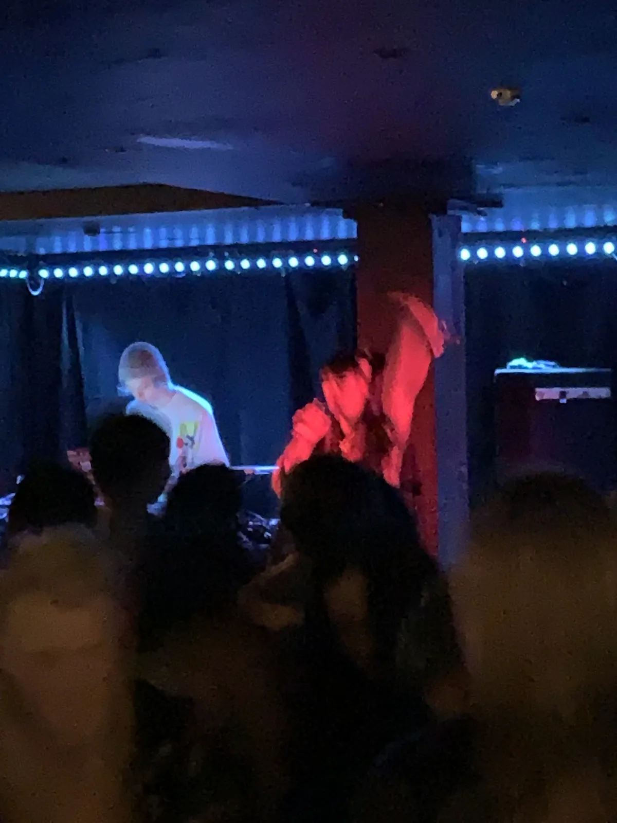 Two performers on a dark stage bathed in blue and red light, LED strip lighting the ceiling