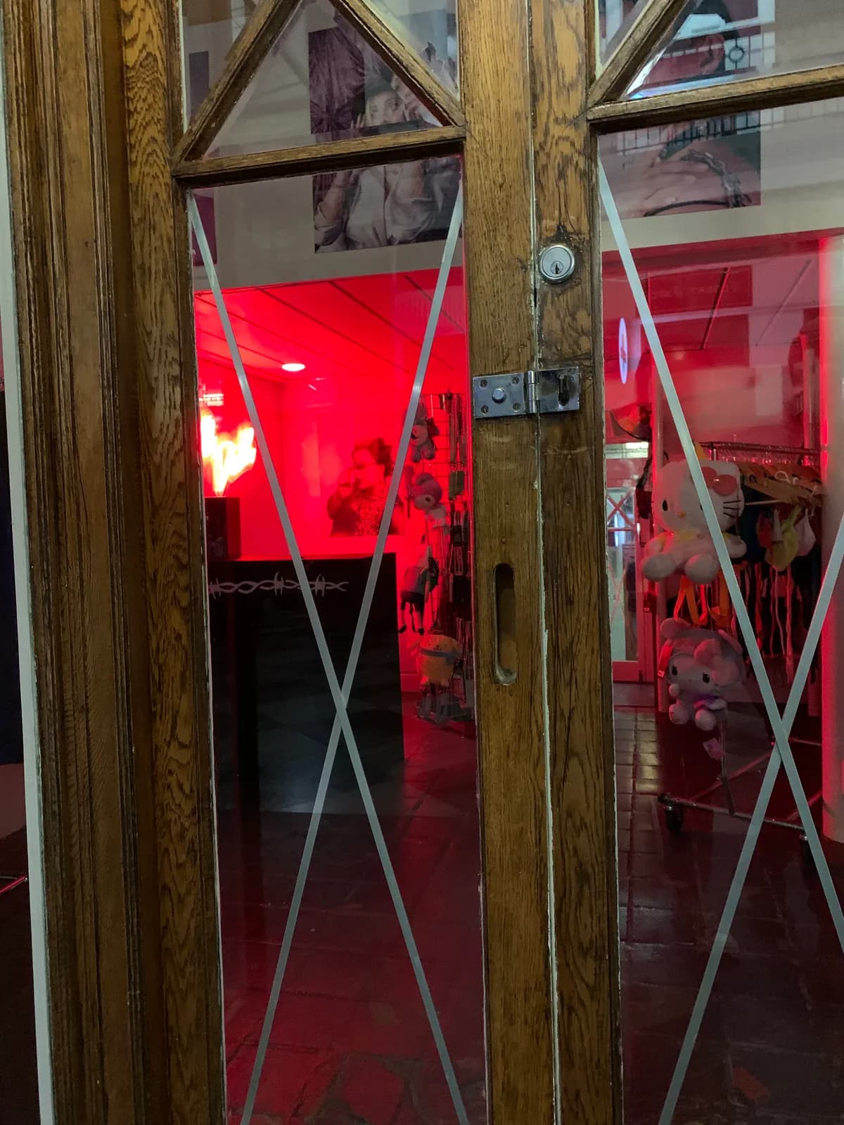 A mysterious doorway with cross-pattern glass panels glowing deep red from the interior, a Hello Kitty figure visible inside